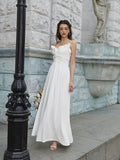 Woman in a white maxi dress with ruffled trim and spaghetti straps standing by a lamppost.
