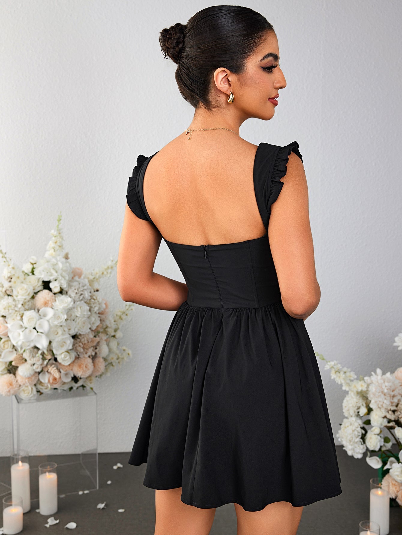 Back view of a woman in a black fit and flare mini dress with ruched cap sleeves