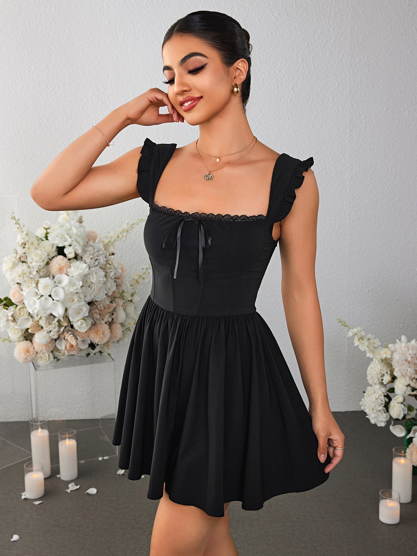 Woman with hand on face wearing a black fit and flare mini dress with ruched cap sleeves