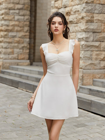 Woman wearing a white satin fit and flare dress with ruffled straps and a ruched sweetheart neckline, posing outdoors.