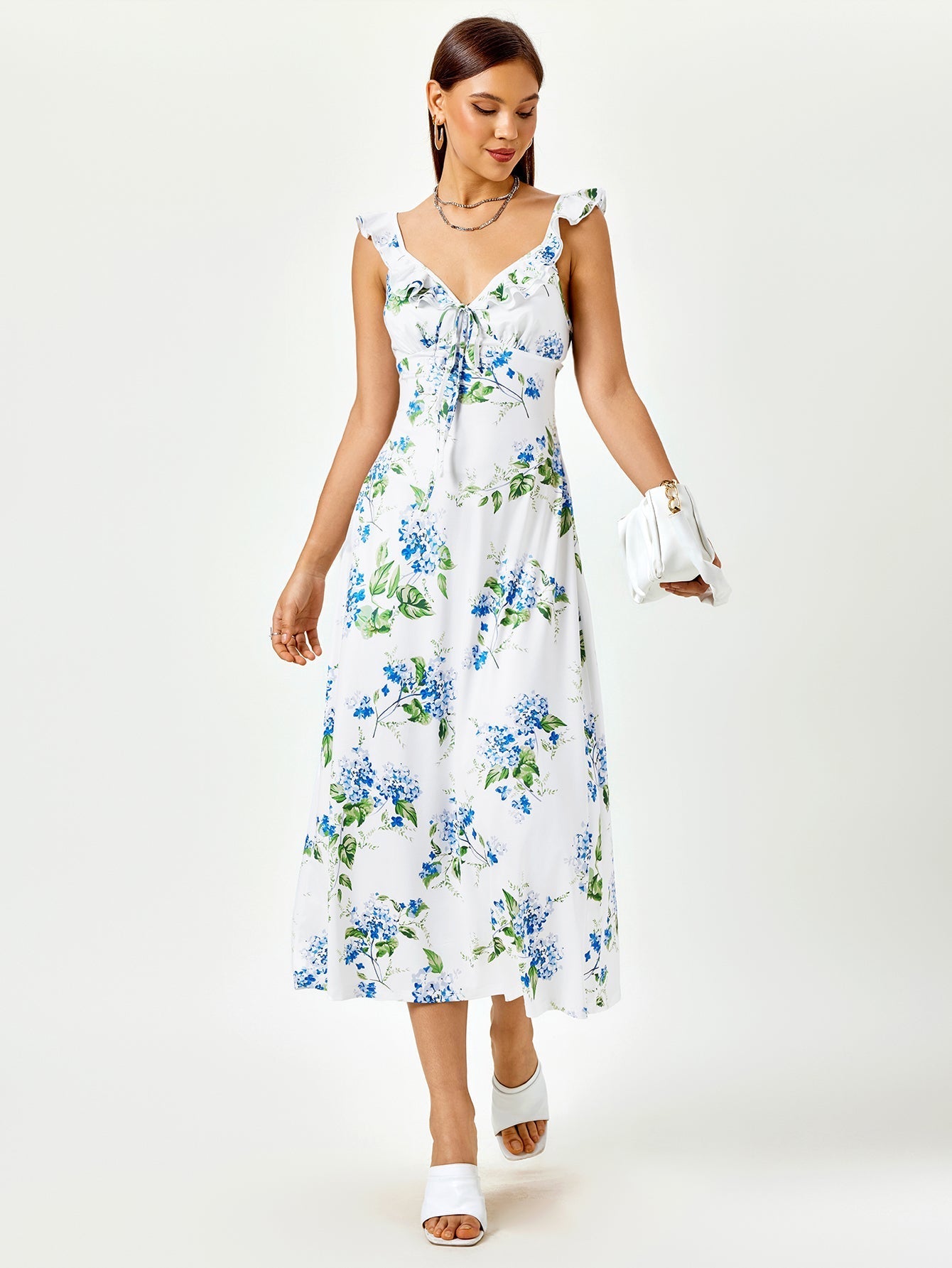 Woman wearing a white midi dress with a blue floral print, featuring ruffled straps and a tie-front detail.