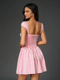Back view of a woman in a pink and white gingham check dress with a smocked back and pleated skirt.