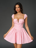 Woman holding the hem of her pink and white gingham check dress, smiling at the camera.
