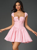 Woman wearing a pink and white gingham check fit and flare dress with a plunging neckline and cap sleeves.