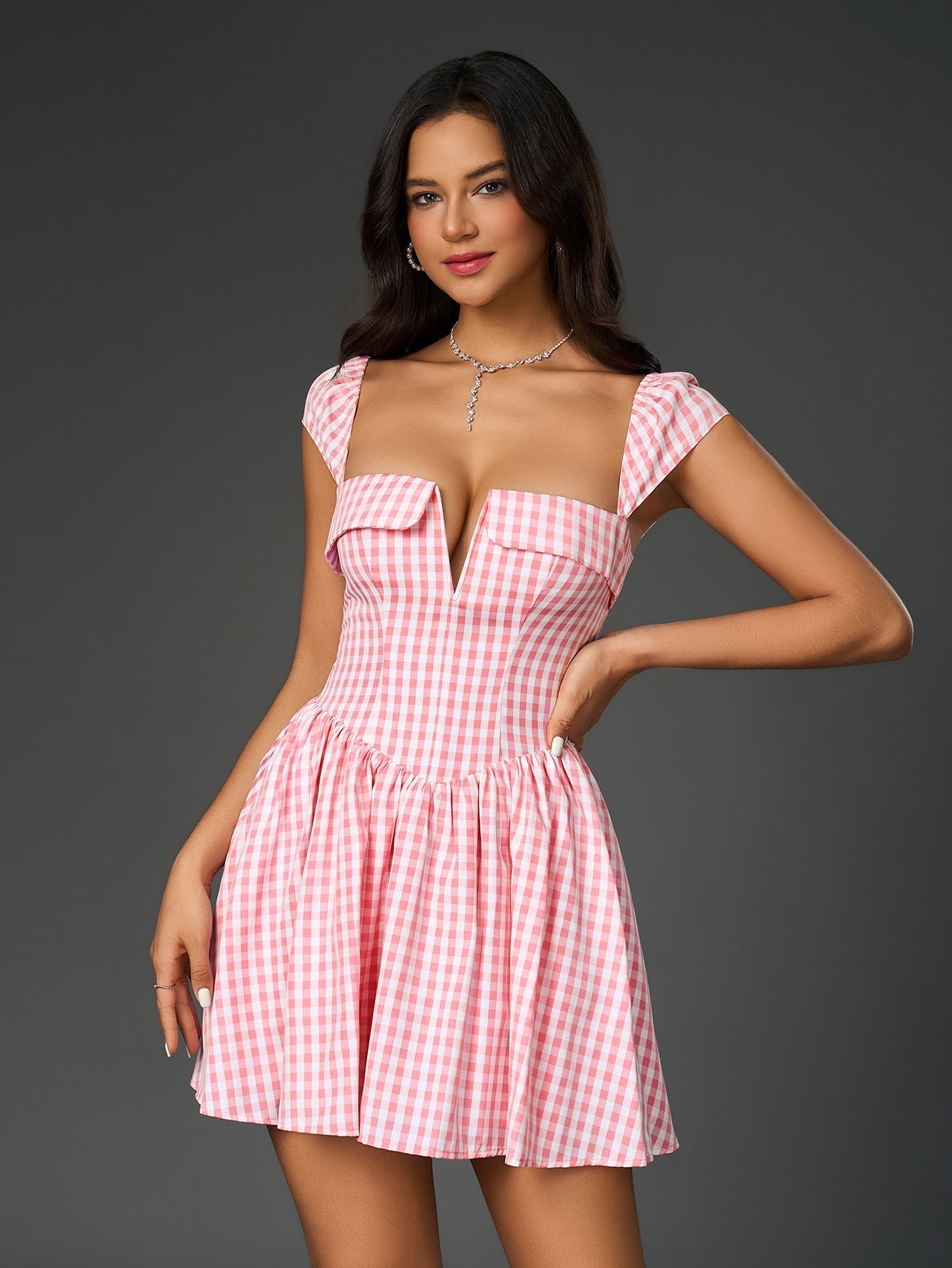 Woman posing in a pink and white gingham check fit and flare dress with her hand on her hip.