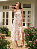 Woman posing in a floral print halter neck midi dress with a high slit in a garden setting.