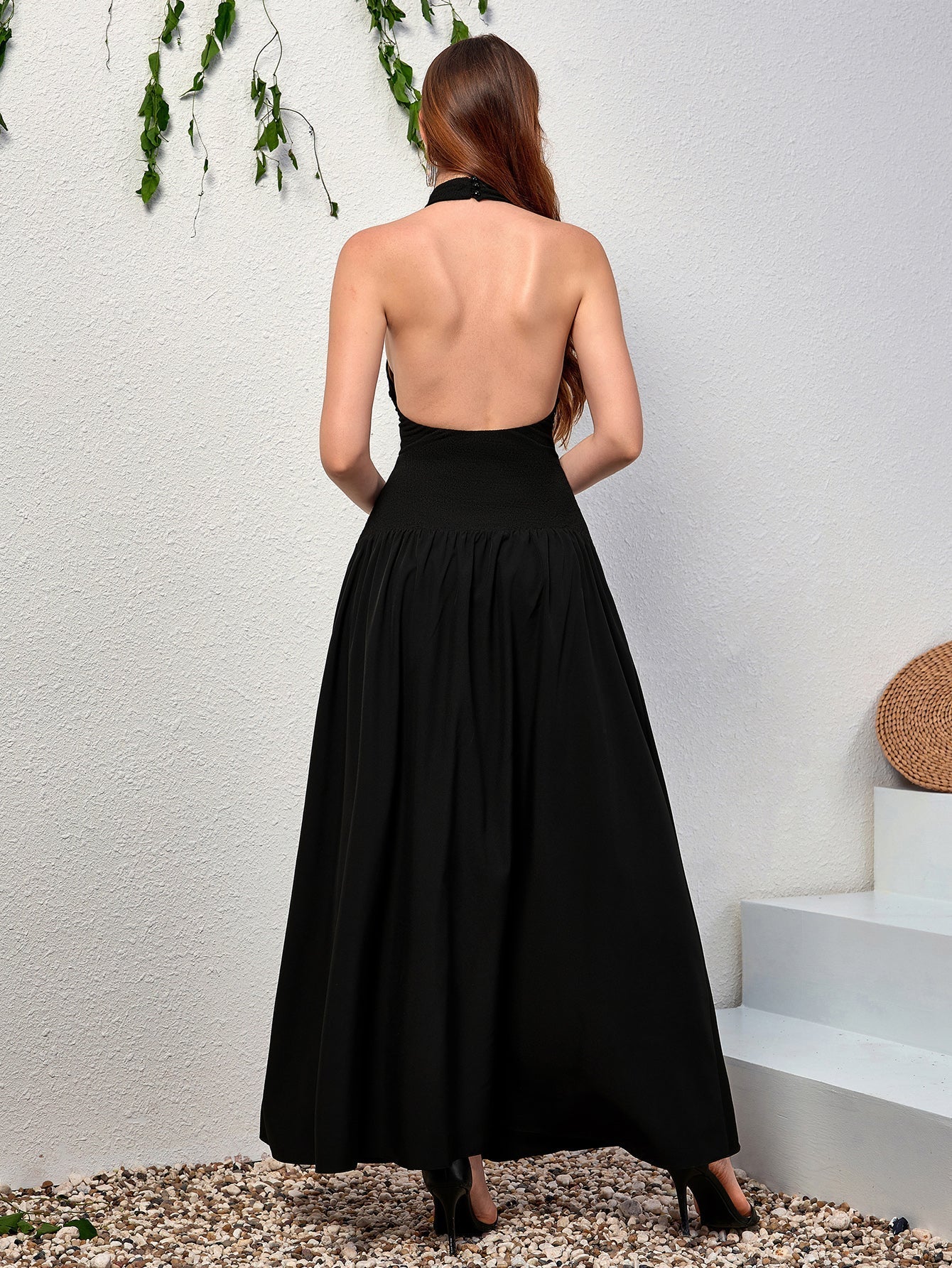 Back view of a woman in a black halter neck maxi dress with an open back.