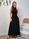 Woman wearing a black sleeveless halter neck maxi dress with a smocked bodice and flowing skirt.