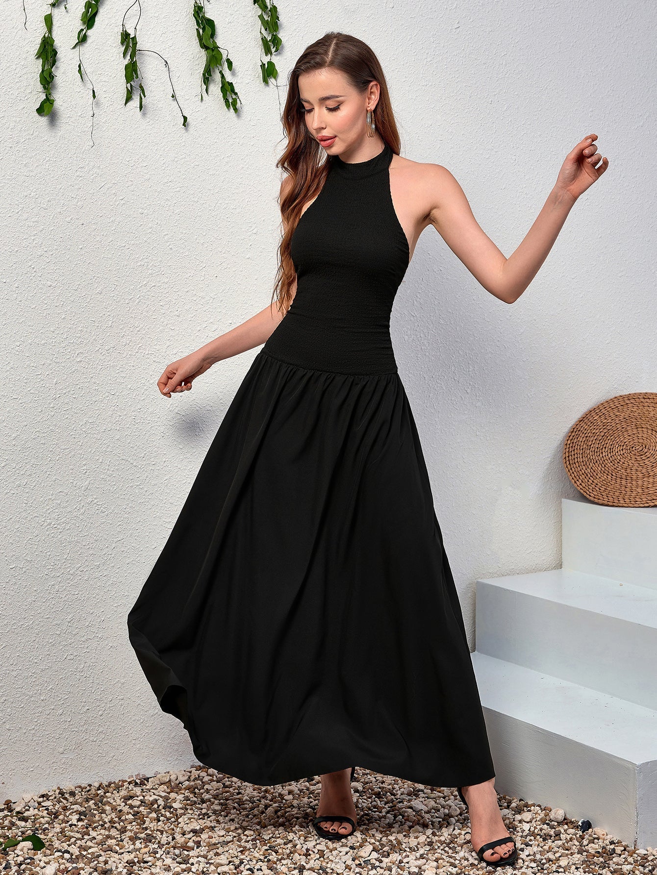 Woman modeling a black halter neck maxi dress, showing the flow of the skirt.