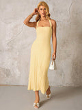 Woman posing in a yellow ribbed knit halter midi dress holding a white handbag.