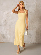 Woman posing in a yellow ribbed knit halter midi dress holding a white handbag.