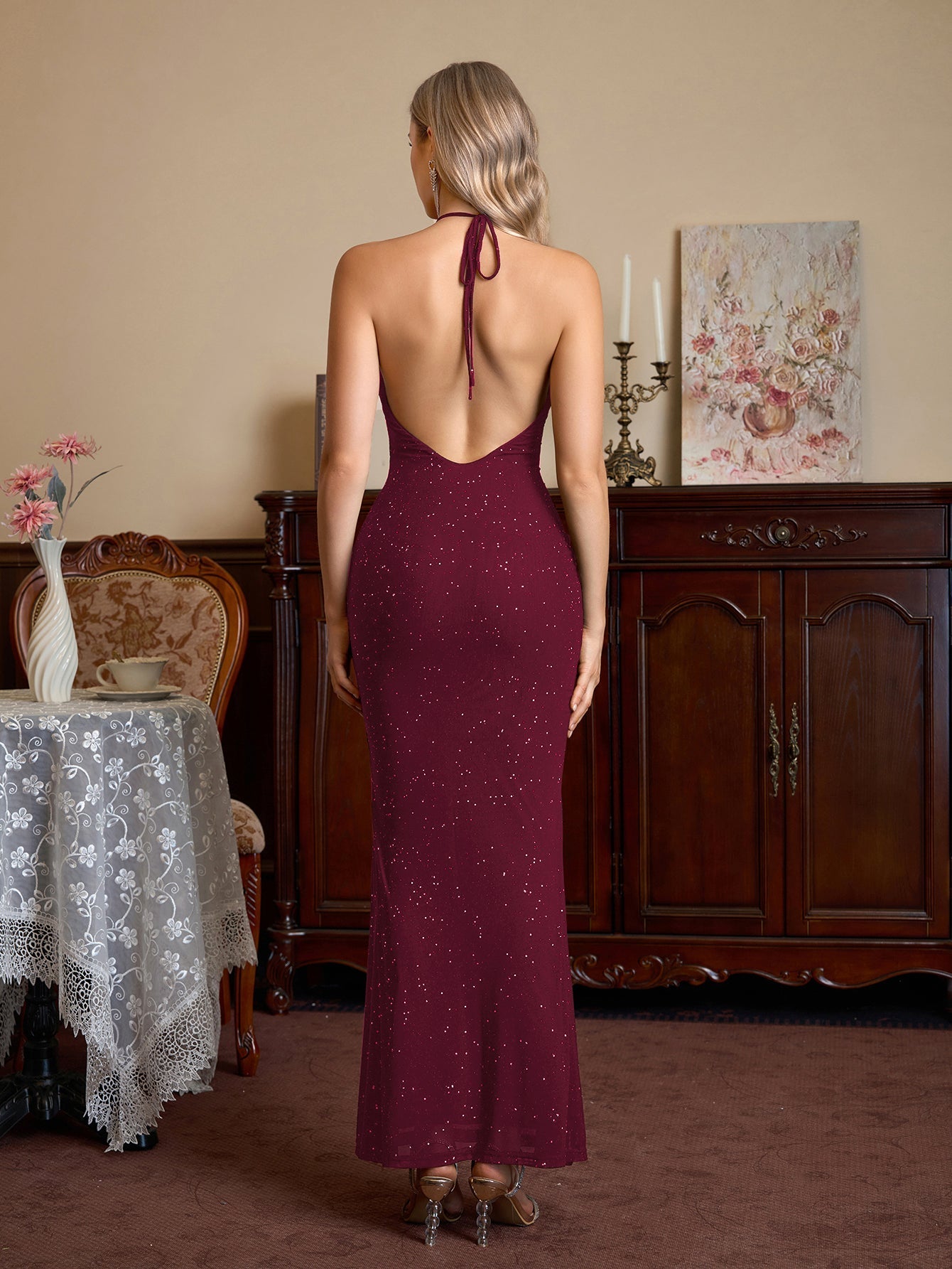 Woman wearing a burgundy sparkling halter neck floor-length trumpet dress, back view.