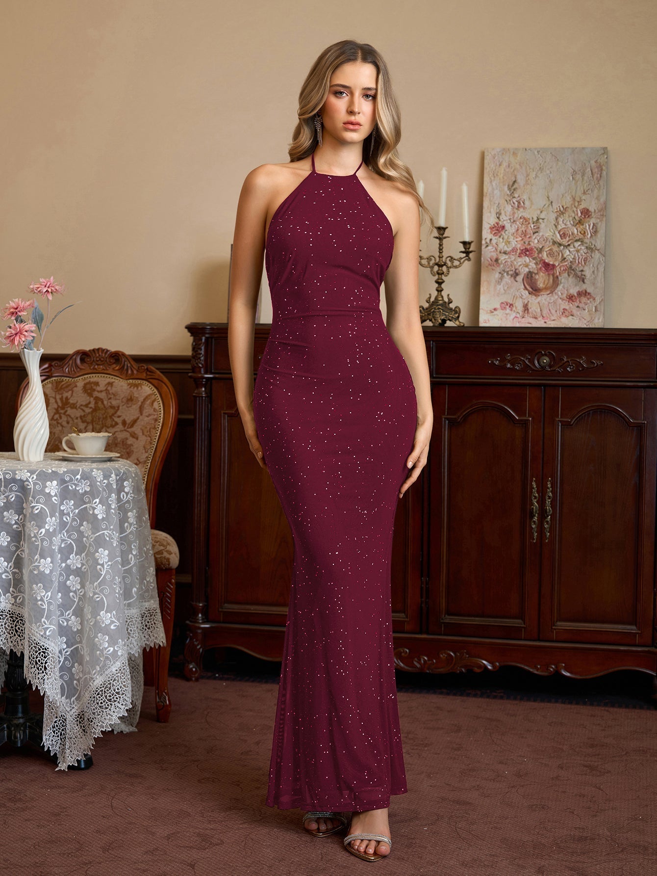 Woman wearing a burgundy sparkling halter neck floor-length trumpet dress, full length view.