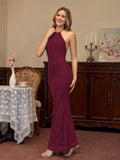 Woman wearing a burgundy sparkling halter neck floor-length trumpet dress, side view.