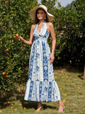 Woman wearing a blue and white patterned maxi dress, halter neckline, and a wide-brimmed straw hat, holding an orange