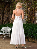 Back view of a woman in a white halter maxi dress with an open back tied with a bow.