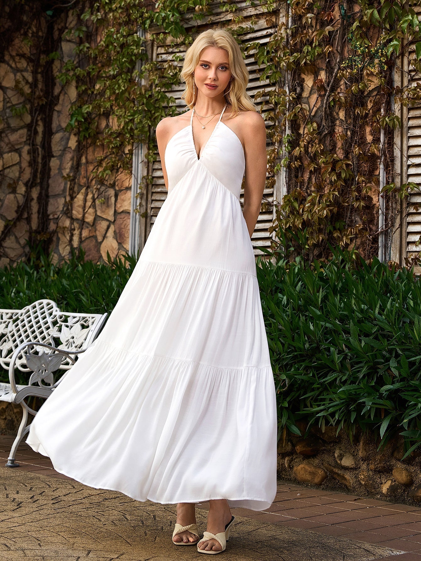 Woman wearing a white halter maxi dress with a tiered skirt in an outdoor setting.