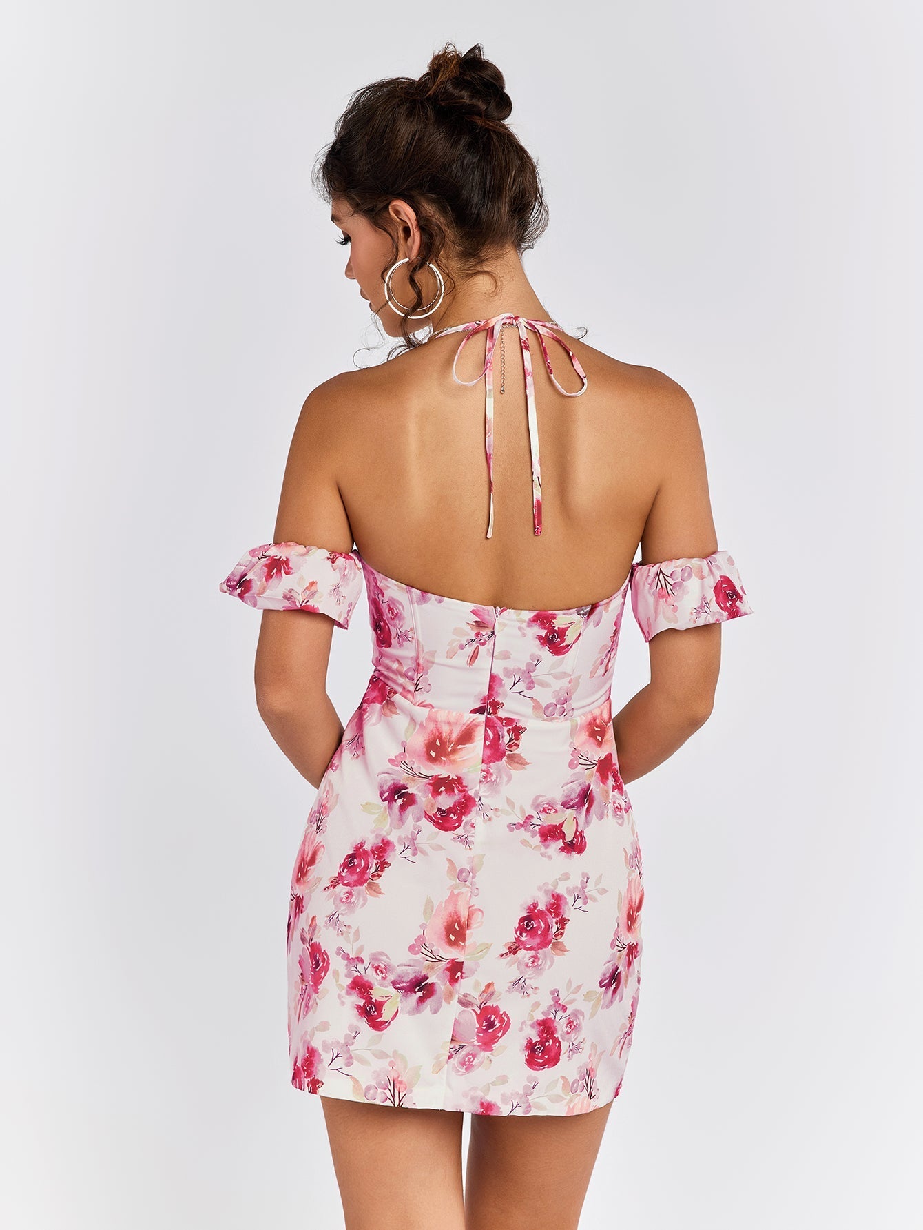 Back view of a woman in a white floral print mini dress with off-the-shoulder sleeves and a halter tie closure.