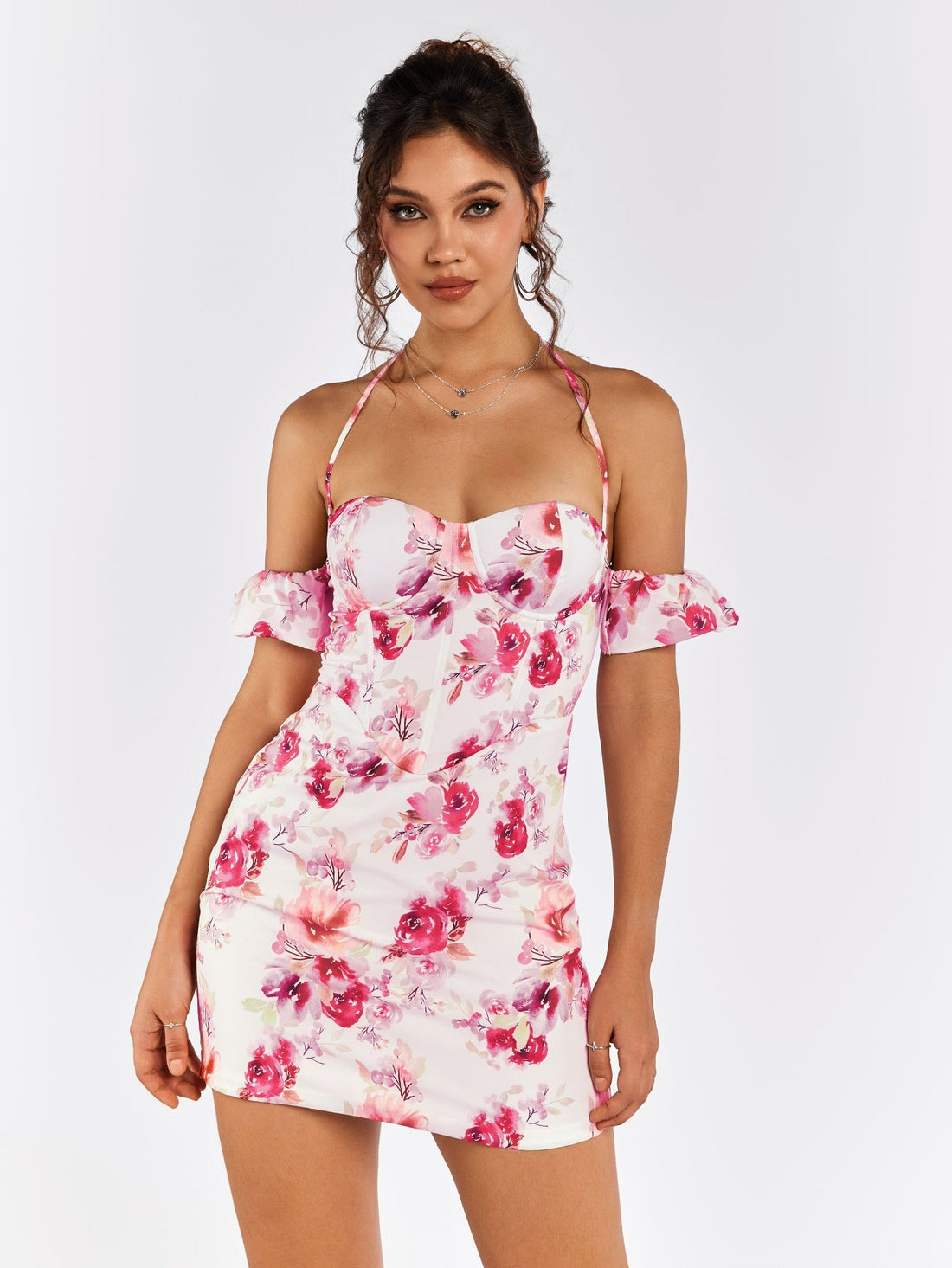 Woman wearing a white mini dress with a pink floral print, featuring an off-the-shoulder design and halter neckline.