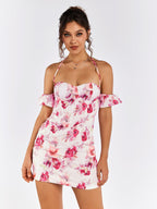 Woman wearing a white mini dress with a pink floral print, featuring an off-the-shoulder design and halter neckline.