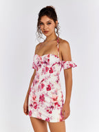 Full body shot of a woman posing in a white floral print mini dress with off-the-shoulder sleeves and halter neckline.