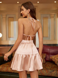 Back view of a woman in a pink satin halter neck mini dress with an open back and tie detail.