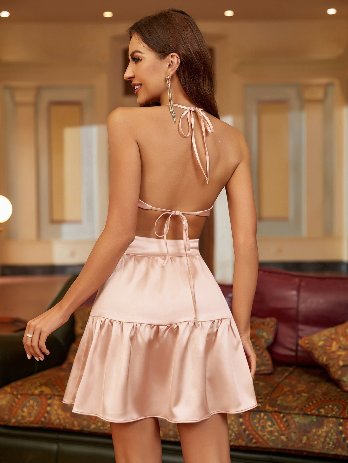 Back view of a woman in a pink satin halter neck mini dress with an open back and tie detail.