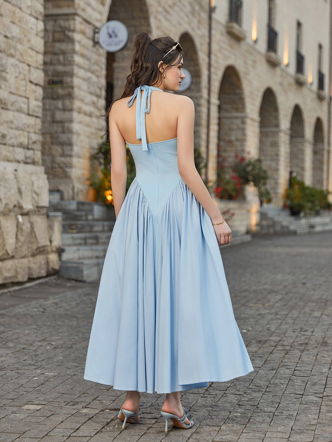 Woman wearing a light blue halter neck midi dress with a pleated skirt