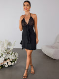 Full body shot of a woman in a black halter mini dress with lace and ruffles, posing with hand on chest