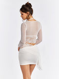 Back view of a woman in a white sheer mesh top and white ruched mini skirt.