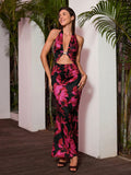 Woman in a black and pink floral print halter maxi dress with a cut-out detail and gold hardware, smiling and looking to the side.