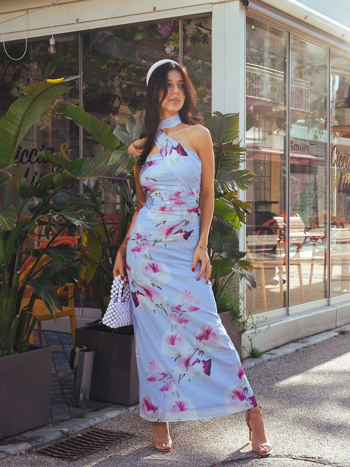 Woman wearing a light blue maxi dress with a large pink and white floral print, featuring a halter neckline and draped detailing.