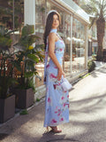Side view of a woman in a light blue floral print maxi dress, showcasing the halter neckline and elegant silhouette.