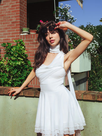 Woman in white asymmetrical dress with scarf detail standing outdoors