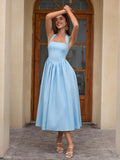 Woman with arms raised above her head in a light blue halter neck midi dress, smiling.