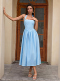 Woman leaning against a pillar in a light blue halter neck midi dress, posing.