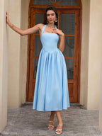 Woman leaning against a pillar in a light blue halter neck midi dress, posing.