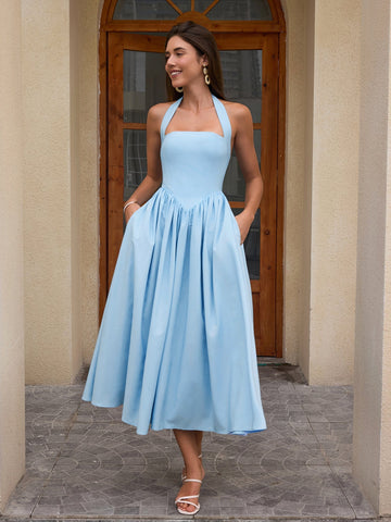 Woman wearing a light blue halter neck midi dress with pockets, standing outdoors.