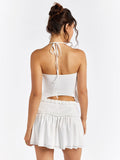 Back view of a woman in a white halter crop top and a white tiered mini skirt with a ruffled waistband.