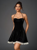 Woman wearing a black velvet halter neck mini dress with a ruched bodice and a white sheer hem trim, front view.