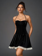 Woman wearing a black velvet halter neck mini dress with a ruched bodice and a white sheer hem trim, front view.