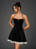Woman wearing a black velvet halter neck mini dress with a ruched bodice and a white sheer hem trim, posing with hands behind back.