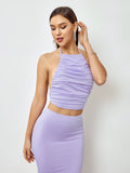 Woman posing in a lavender ruched halter crop top and mermaid maxi skirt, showing off jewelry