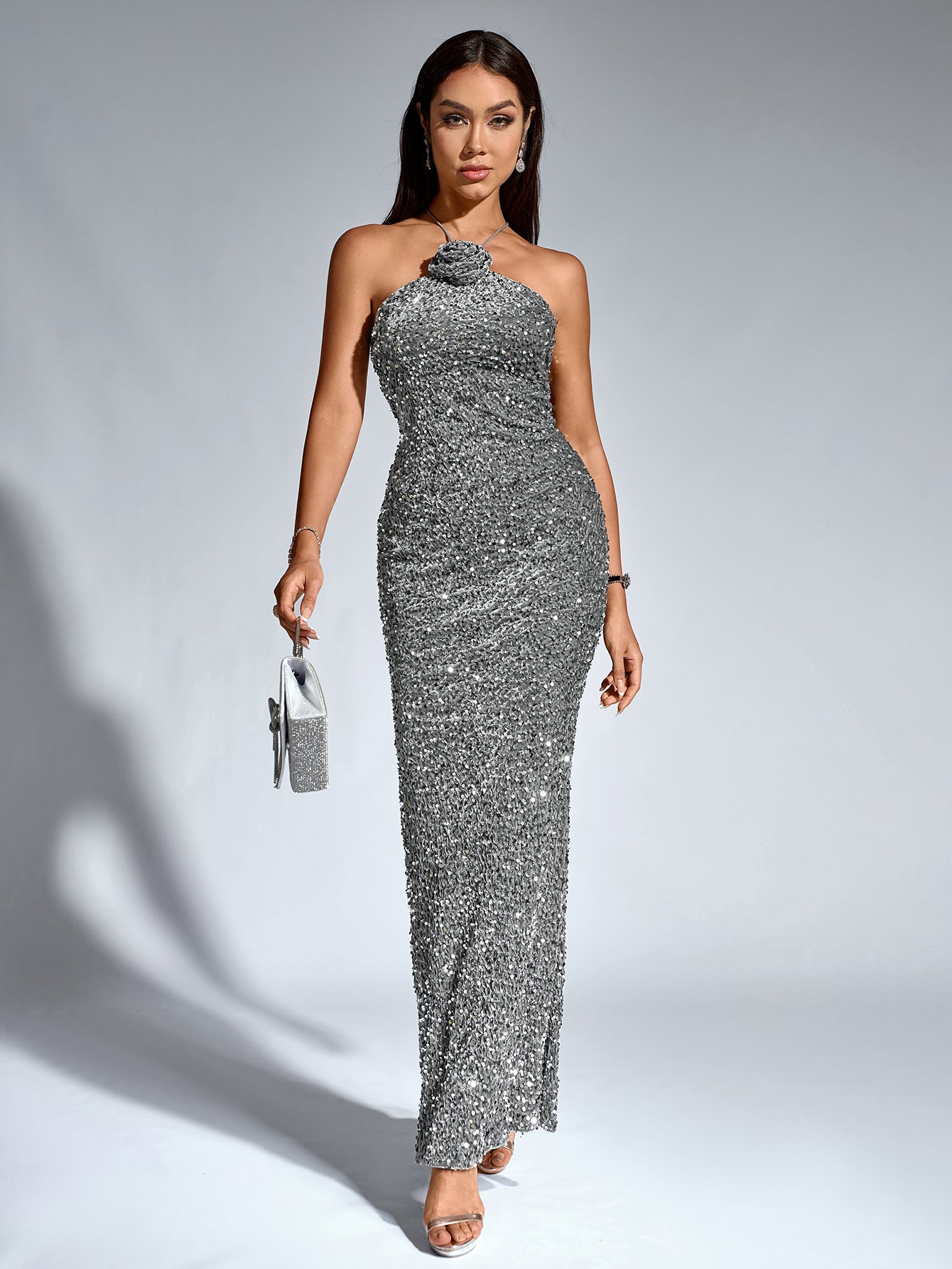 Woman holding a small silver sequined clutch while wearing a silver sequined halter neck mermaid gown