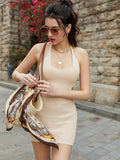 Woman accessorizing with a straw bag and scarf while wearing a beige crochet knit halter mini dress.