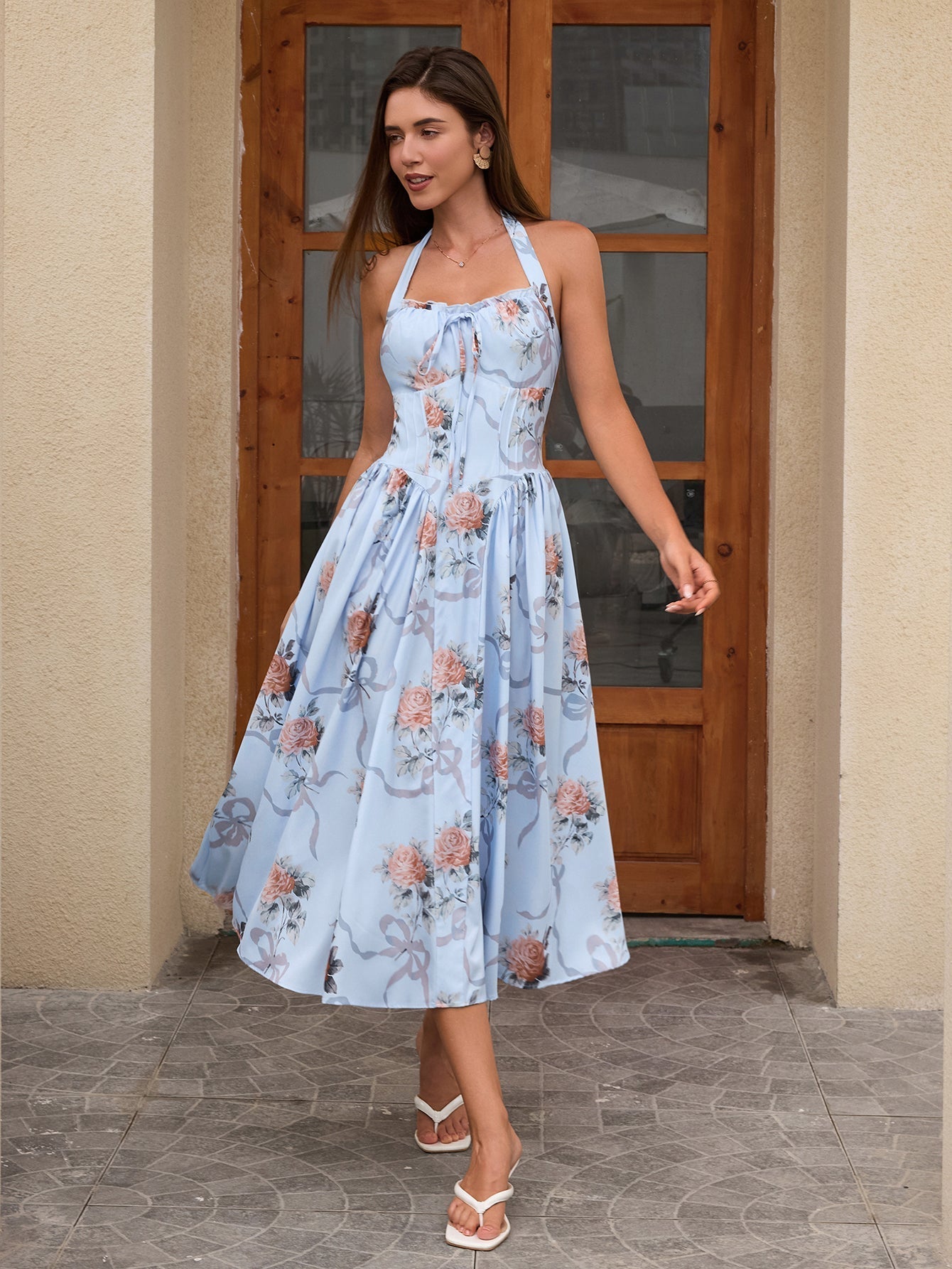 Woman twirling in a light blue floral print halter neck midi dress with a flared skirt in front of a doorway.