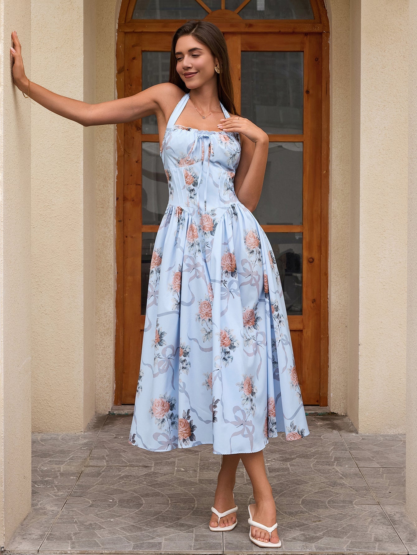 Woman posing in a light blue floral print halter neck midi dress with a flared skirt against a doorway.