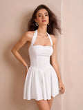 Woman in a white halter neck dress leaning against a wall