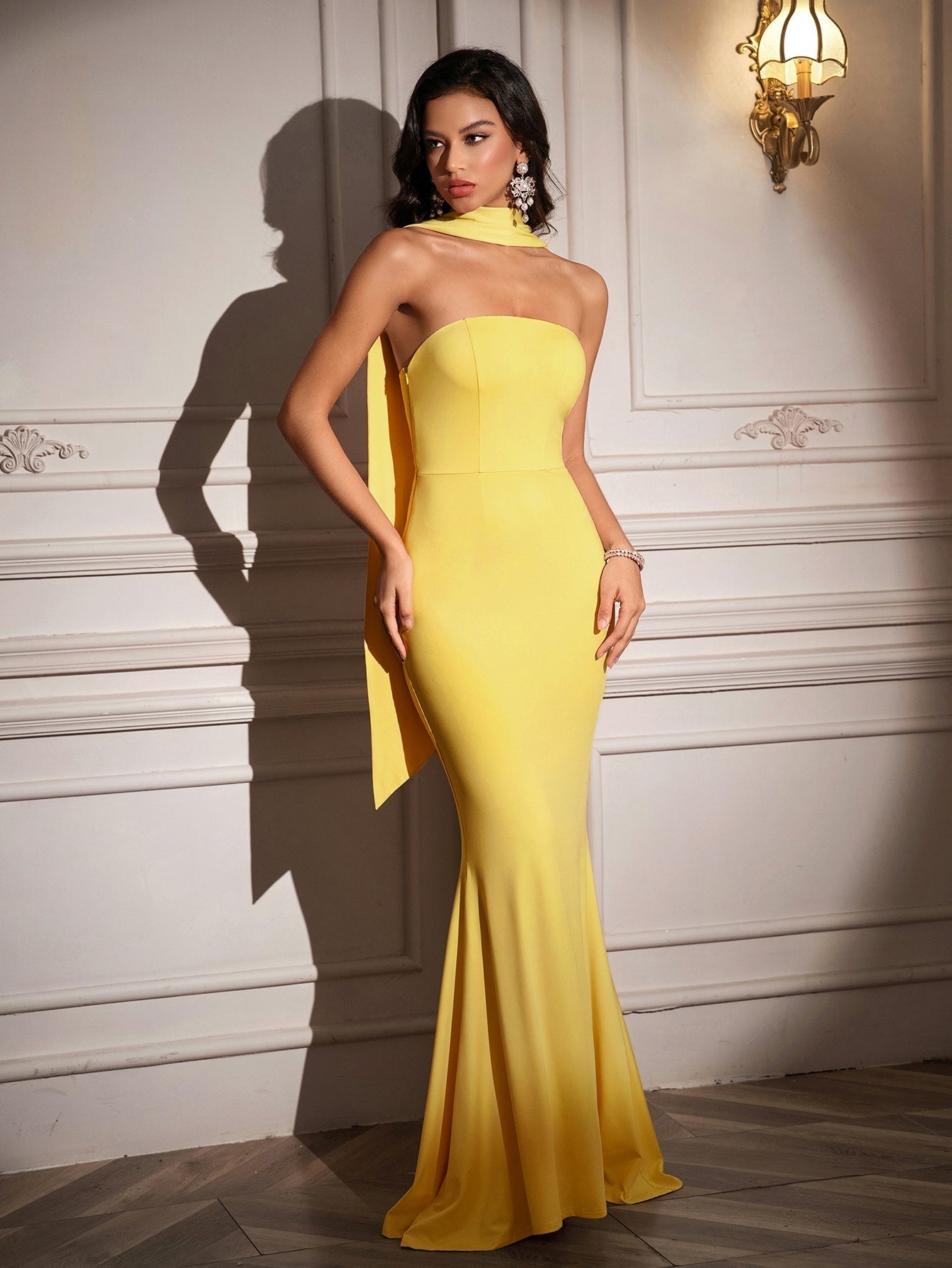 Model posing in a yellow strapless mermaid dress with a high neckline scarf.