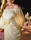 Model posing in a flowing cream satin dress with an off-the-shoulder neckline and lantern sleeves.